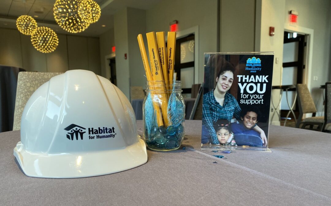 A hard hat with the Habitat Greater Boston logo sits on a table next to a sign that says "thank you" above a picture of a smiling family